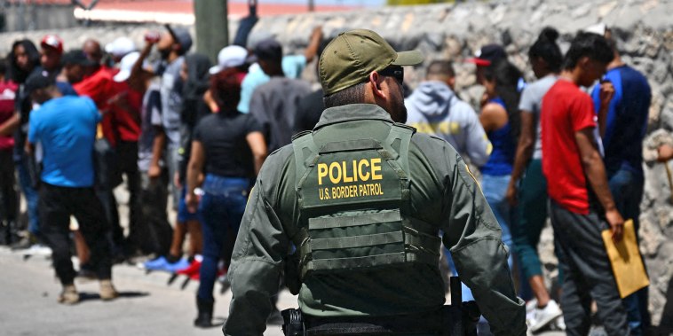 A Border Patrol agent walks along a line of migrants waiting to turn themselves in for processing, in El Paso, Texas